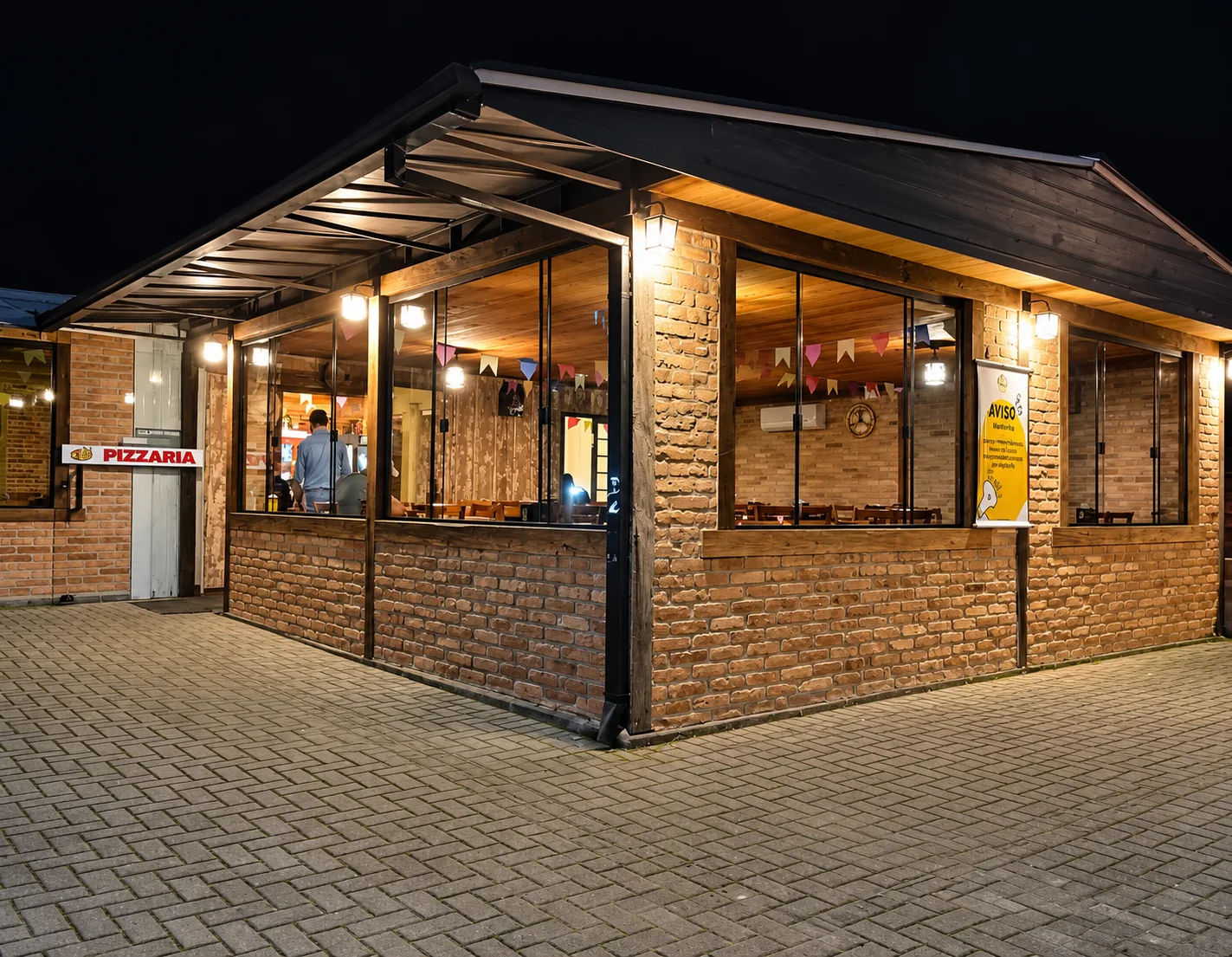 Fachada da Lanchonete e Pizzaria 20V à noite, com estrutura de tijolo aparente e madeira